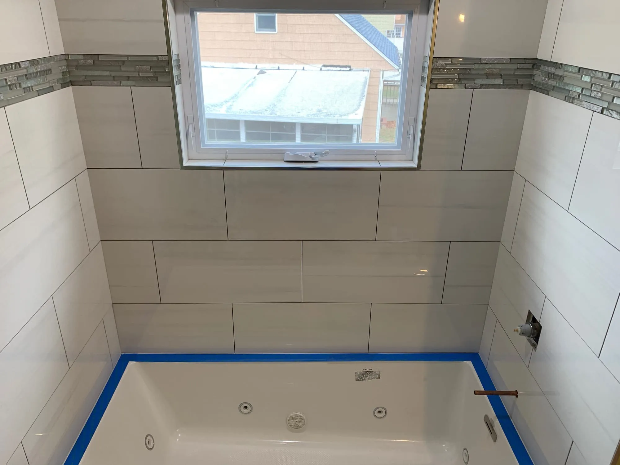 Whirlpool tub installed with large-format white wall tile and a glass mosaic accent band
