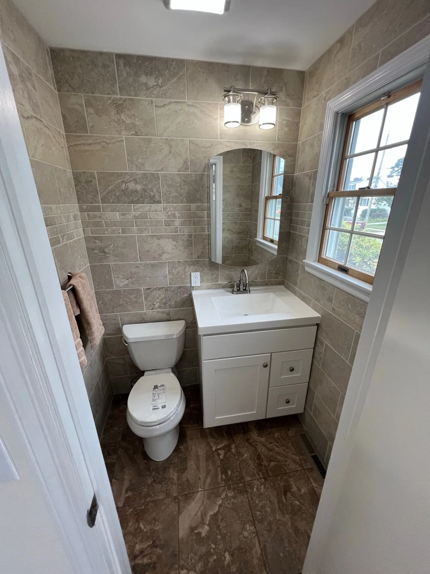 Powder room with a white vanity and arched mirror beside a window