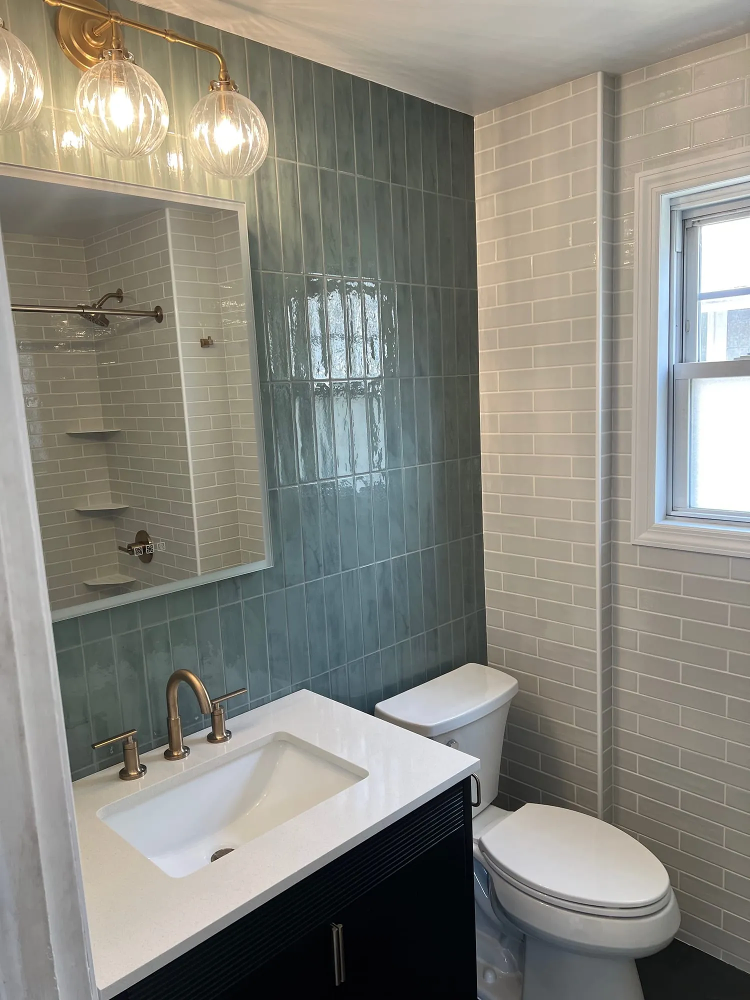 Vanity wall with sage tile, a globe light fixture and brass faucet beside a window