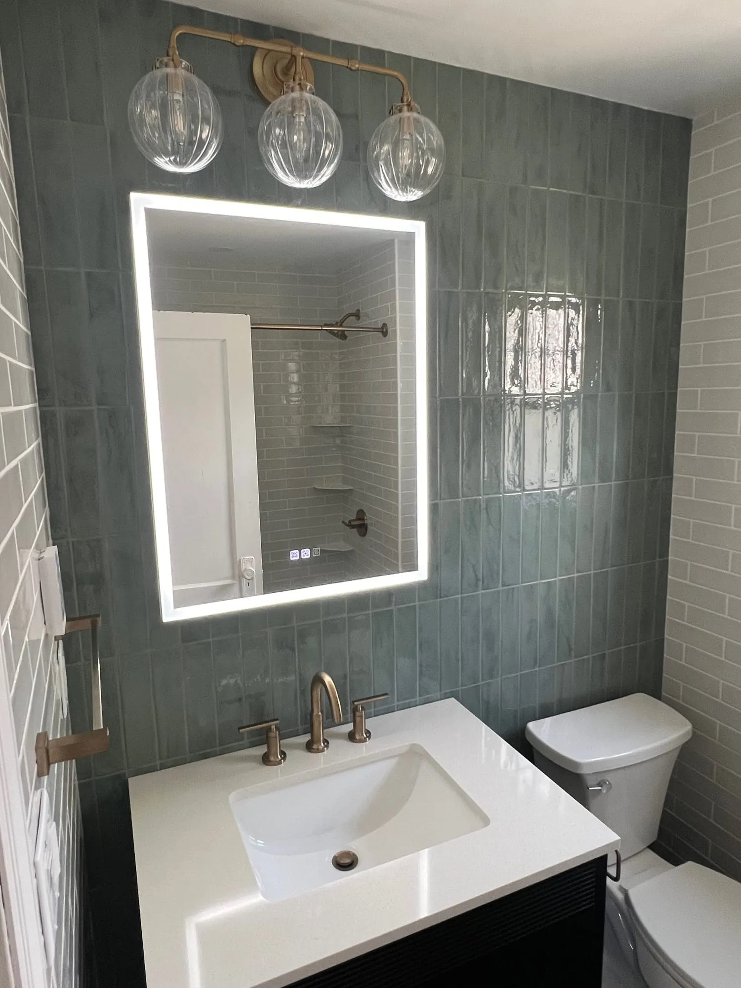 Lighted mirror over a white-topped vanity against glossy sage tile
