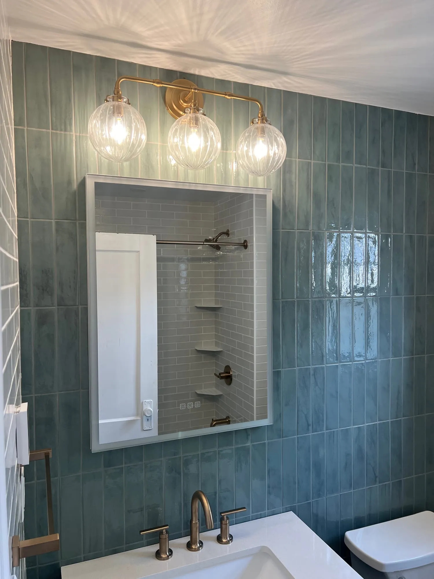 Brass globe vanity light over a mirror and sage tile accent wall