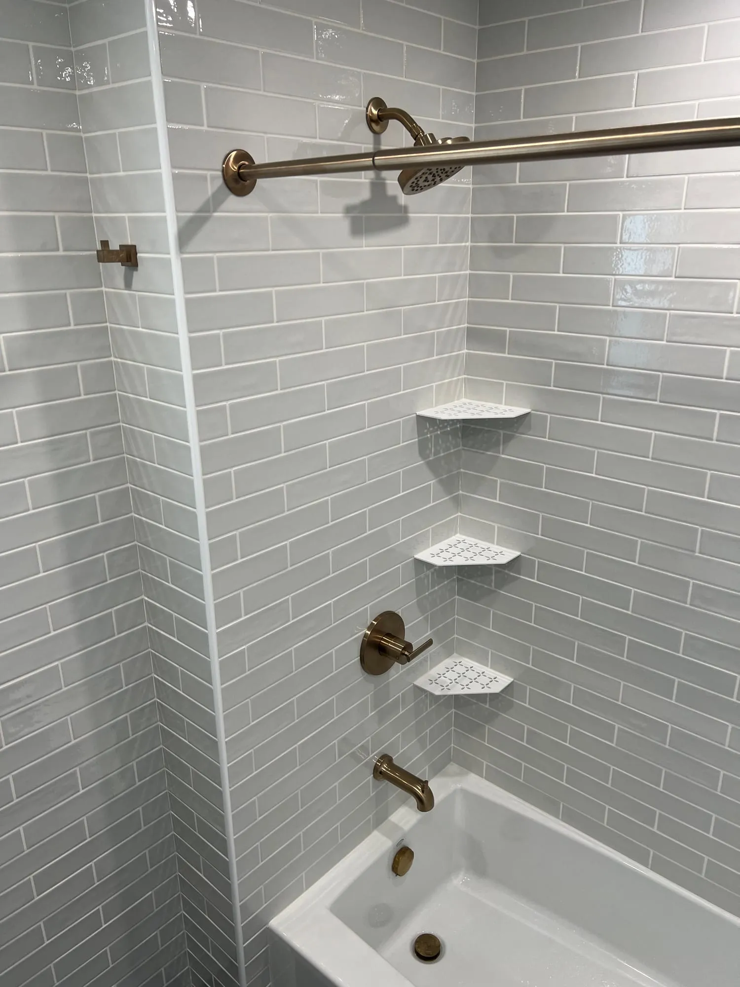 Brass shower head, valve and tub spout on gray subway tile