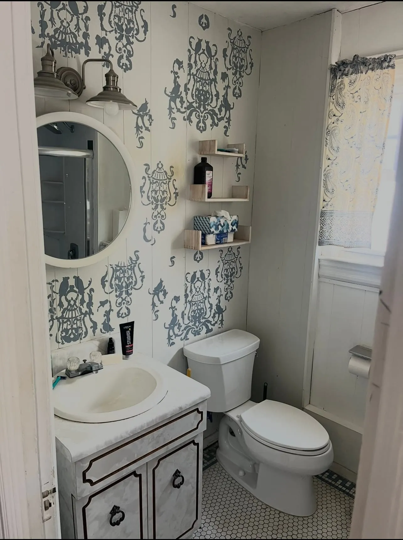 The bathroom before renovation, with patterned wallpaper and an older vanity