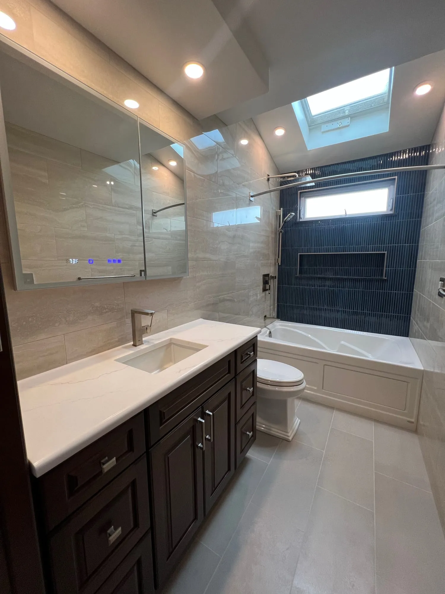 The same bathroom after, with a dark vanity, backlit mirror and navy tile beyond