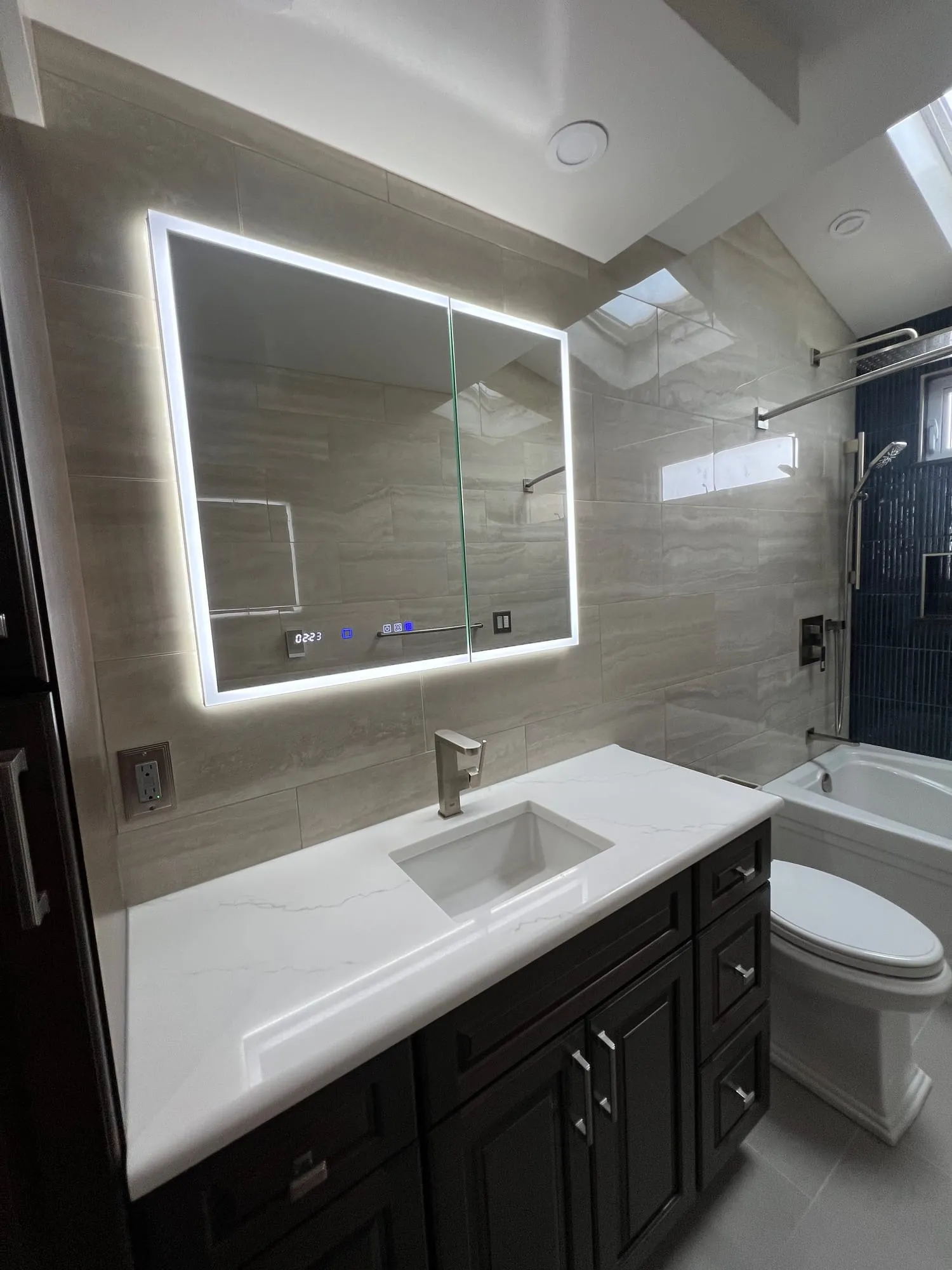 Backlit mirror over a dark raised-panel vanity with a white countertop