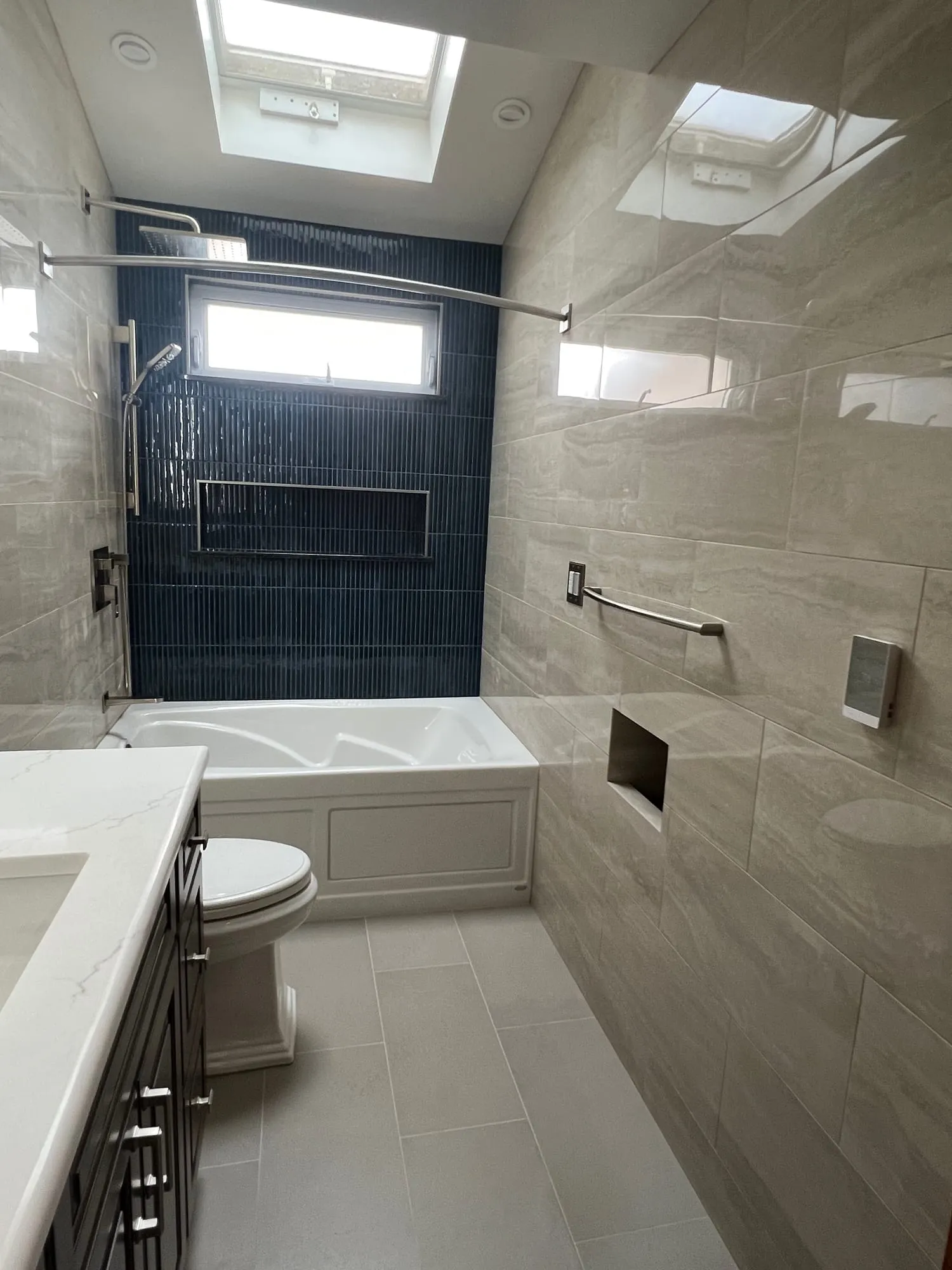Full view of the bathroom with warm gray wall tile, a grab bar and the navy tile tub wall