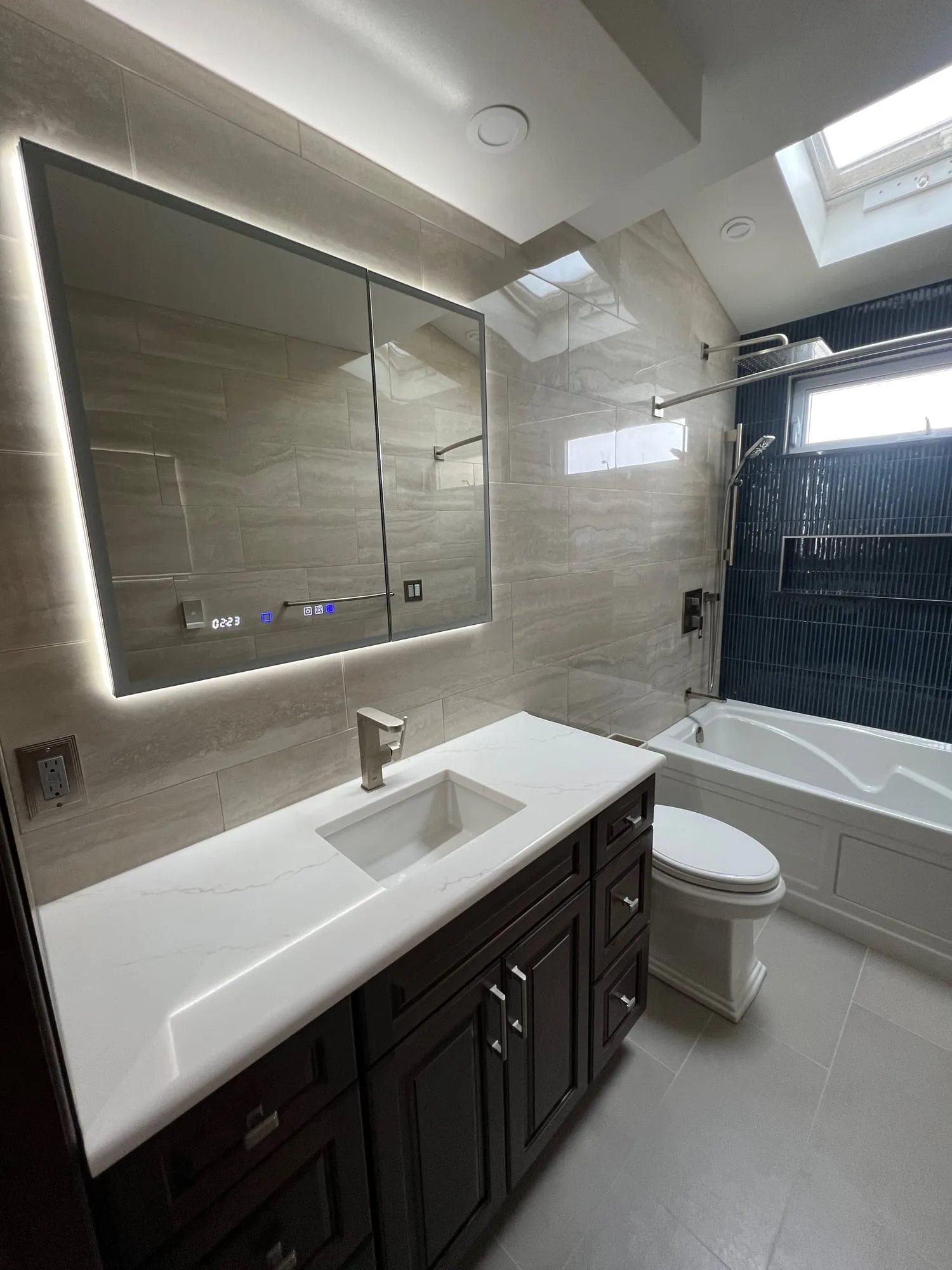 Vanity, toilet and tub wall with navy accent tile under a skylight