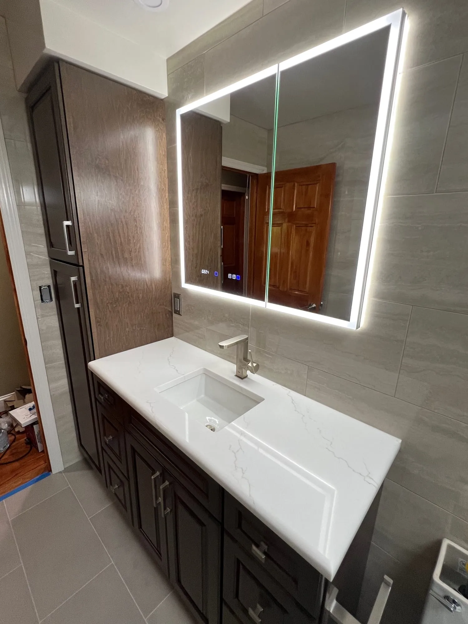 Vanity with a backlit mirror beside a tall wood linen cabinet